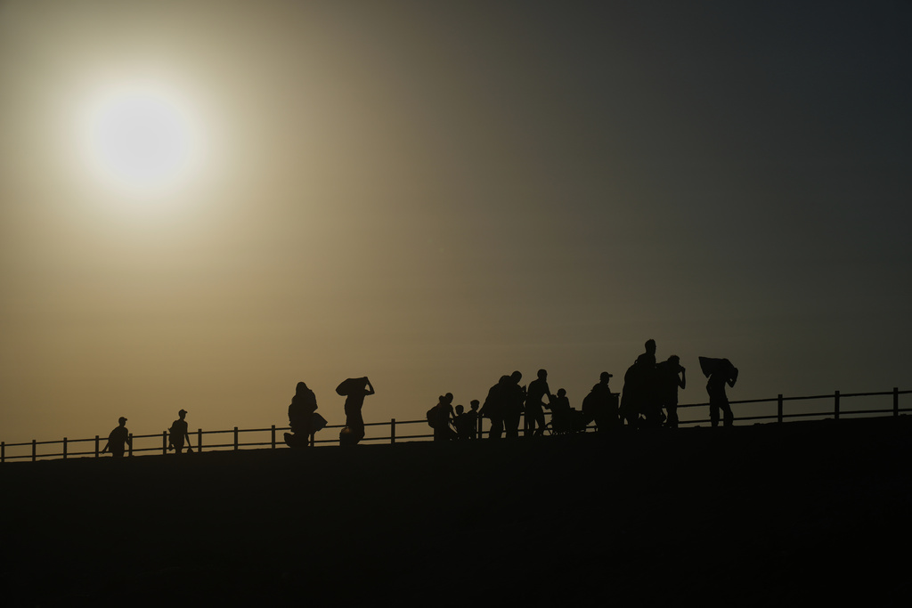 Displaced Palestinians carrying their belongings walk along the coastal road near Wadi Gaza in the central Gaza Strip at sunset, Friday, Oct. 10, 2025, after Israel and Hamas agreed to a pause in their war and the release of the remaining hostages. (AP Photo/Abdel Kareem Hana)