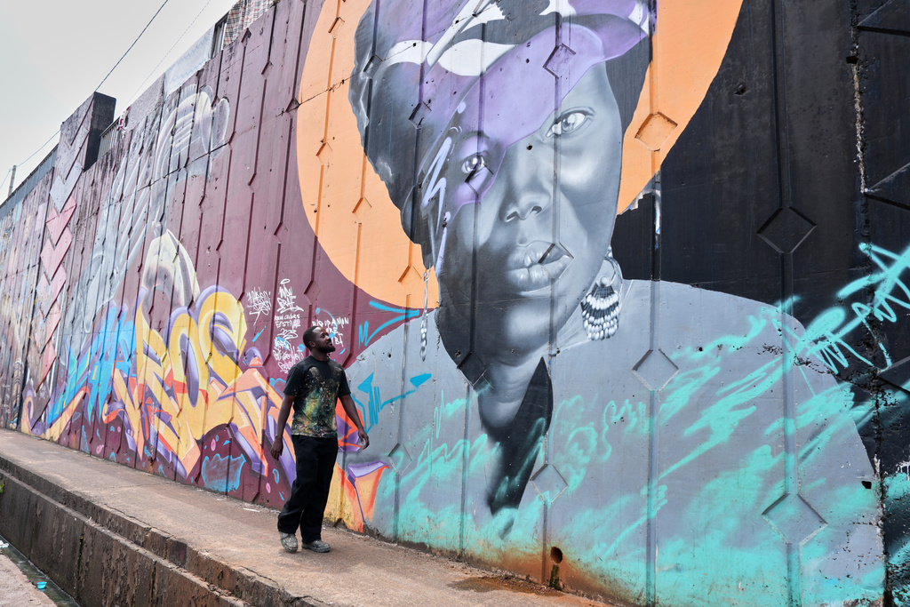Graffiti artist Omar Diaw walks past one of his murals on a street wall in Conakry, Guinea, Saturday, Sep. 20, 2025. (AP Photo/Misper Apawu)