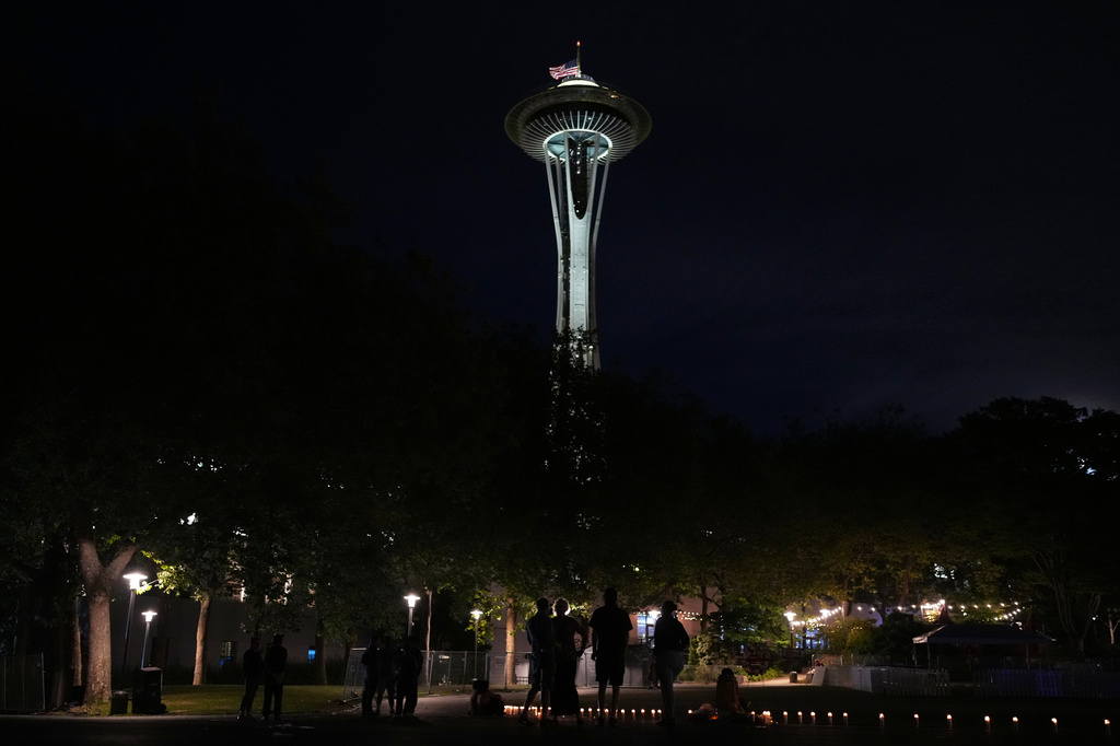 With a backdrop of the Space Needle, people are silhouetted after the vigil for victims the day after a shooting at Seattle Center during the Bite of Seattle food festival, Monday, July 27, 2026, in Seattle. (AP Photo/Lindsey Wasson)