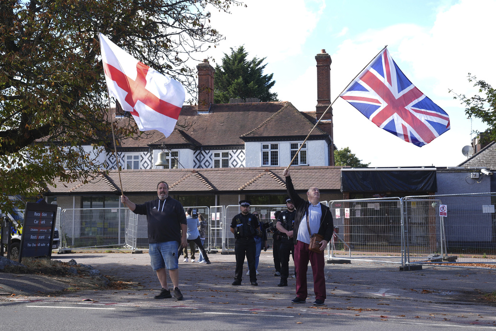 Police officers watch protesters outside the Bell Hotel in Epping, England, Friday, Aug. 29, 2025, after a temporary injunction that would have blocked asylum seekers from being housed at the hotel in was overturned at the Court of Appeal. (Lucy North/PA via AP)