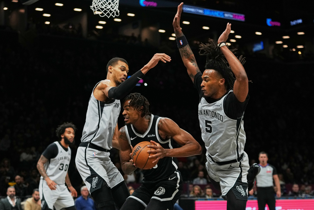 San Antonio Spurs' Victor Wembanyama, left, and Stephon Castle, right, defends Brooklyn Nets' Nic Claxton during the first half of an NBA basketball game Thursday, Feb. 26, 2026, in New York. (AP Photo/Frank Franklin II)