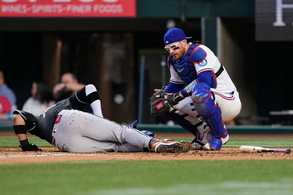 Texas Rangers catcher Danny Jansen kneels by Arizona Diamondbacks' Lourdes Gurriel Jr. who fouled a pitch onto legs in the fourth inning of a baseball game Wednesday, May 13, 2026, in Arlington, Texas. (AP Photo/Tony Gutierrez)