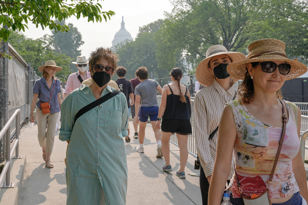 Visitors wear face masks, as smoke from wildfires blankets the sky, Friday, July 17, 2026, in Washington. (AP Photo/Mariam Zuhaib)
