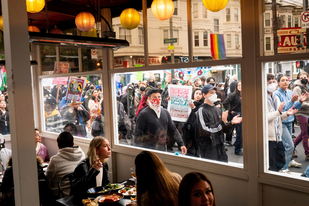 EDS NOTE: OBSCENITY - Protesters against U.S. Immigration & Customs Enforcement raids pass diners while marching through San Francisco's Mission district, June 9, 2025. (AP Photo/Noah Berger, File)