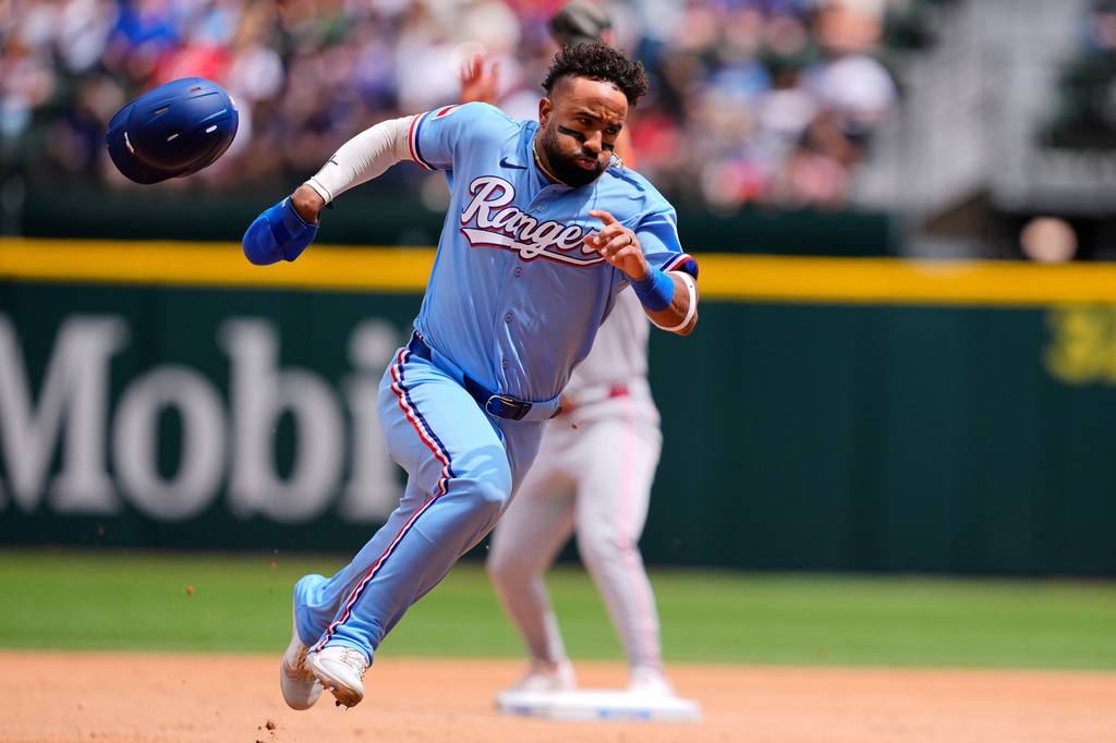 Texas Rangers' Ezequiel Duran loses his helmet rounding second as he advances to third on a single by Brandon Nimmo in the third inning of a baseball game against the Cincinnati Reds Sunday, April 5, 2026, in Arlington, Texas. (AP Photo/Tony Gutierrez)