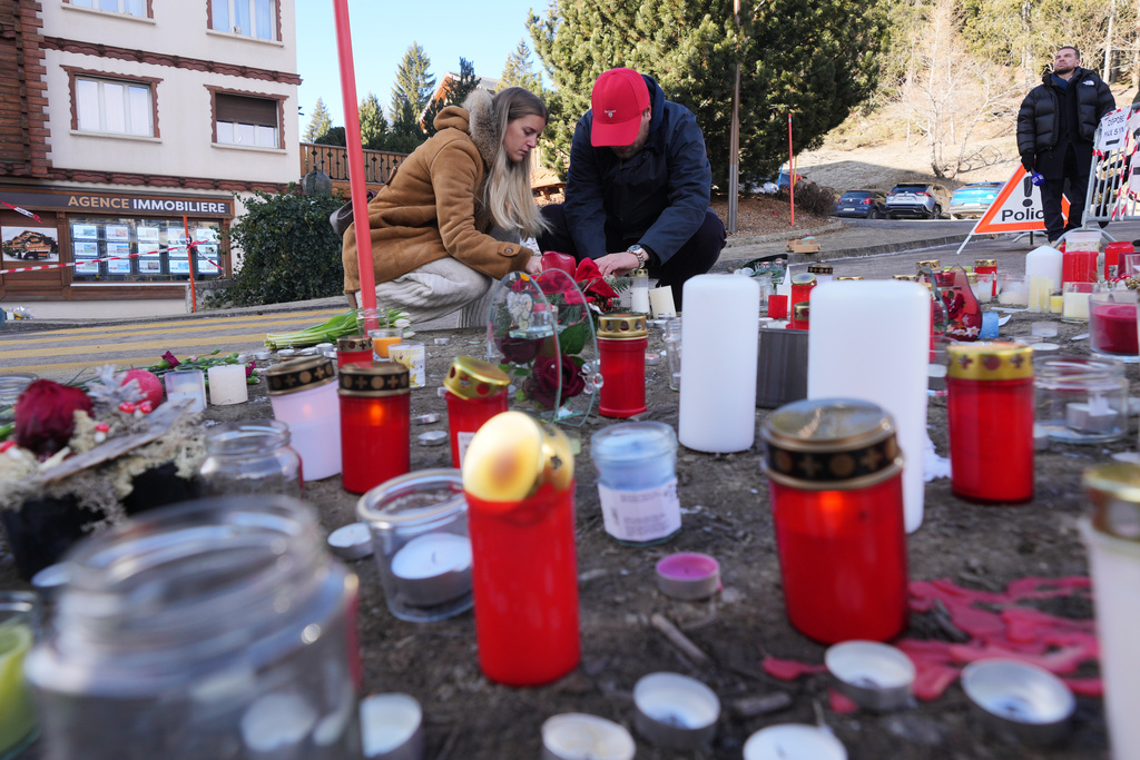 People bring flowers and candles near the sealed off Le Constellation bar, where a devastating fire left dead and injured during the New Year's celebrations in Crans-Montana, Swiss Alps, Switzerland, Friday, Jan. 2, 2026. (AP Photo/ Antonio Calanni)