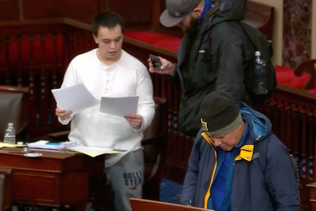 This image from Senate Television shows Christopher Moynihan looking through papers from the desk of a senator in the Senate Chamber at the U.S. Capitol in Washington, Jan. 6, 2021. (Senate Television via AP)