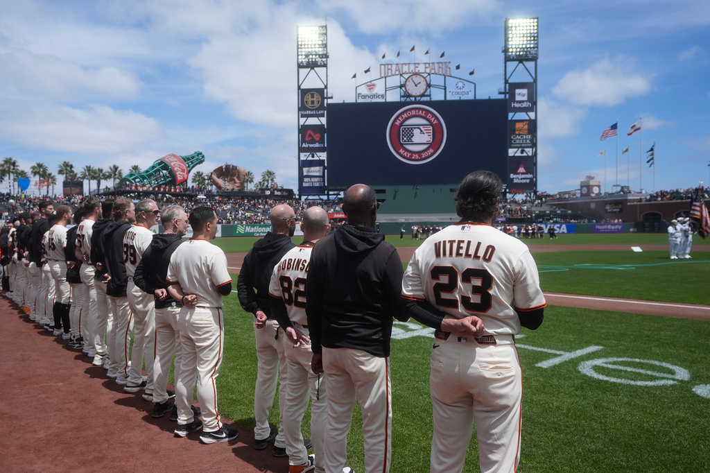 A sign honoring Memorial Day is shown on the videoboard as San Francisco Giants manager Tony Vitello (23) and his team stand for the national anthem before a baseball game between the Giants and the Arizona Diamondbacks Monday, May 25, 2026, in San Francisco. (AP Photo/Jeff Chiu)