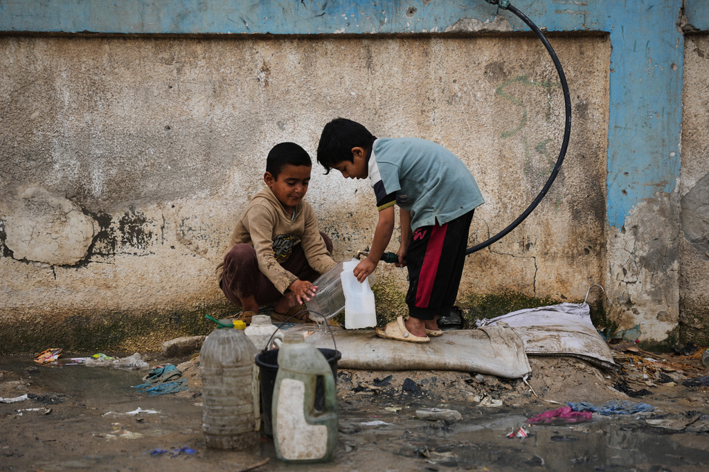 FILE - Palestinian children fill plastic bottles with water at a tent camp in Deir al-Balah, Gaza Strip, Thursday, Jan. 29, 2026. (AP Photo/Abdel Kareem Hana, file)
