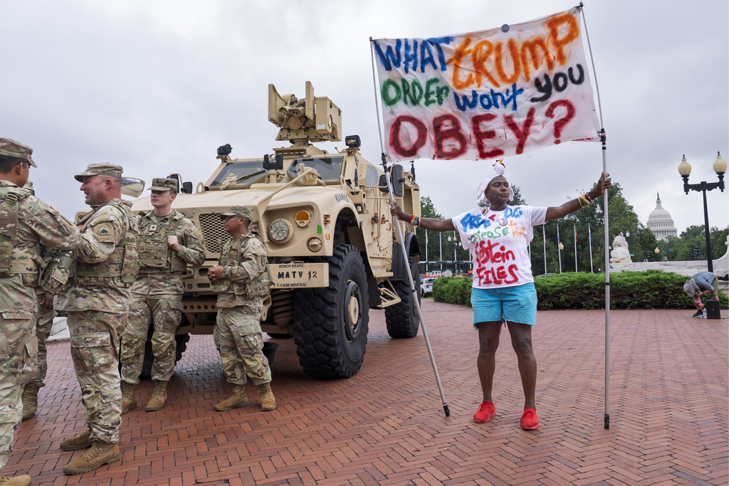 Nadine Seiler of Waldorf, Md., displays her banner as protesters, police, and National Guard troops congregate at the entrance to Union Station in Washington, Wednesday, Aug. 20, 2025. (AP Photo/J. Scott Applewhite)