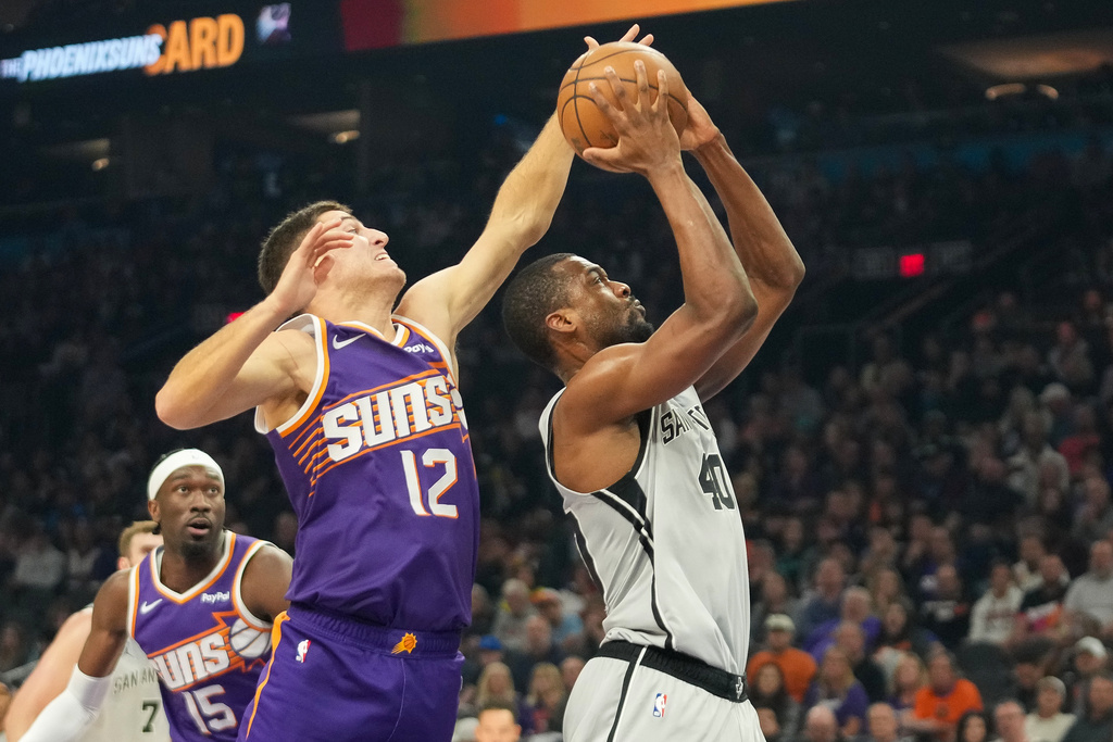 Phoenix Suns guard Collin Gillespie (12) goes for a block on San Antonio Spurs forward Harrison Barnes during the first half of an NBA basketball game in Phoenix, Sunday, Nov. 23, 2025. (AP Photo/Darryl Webb)