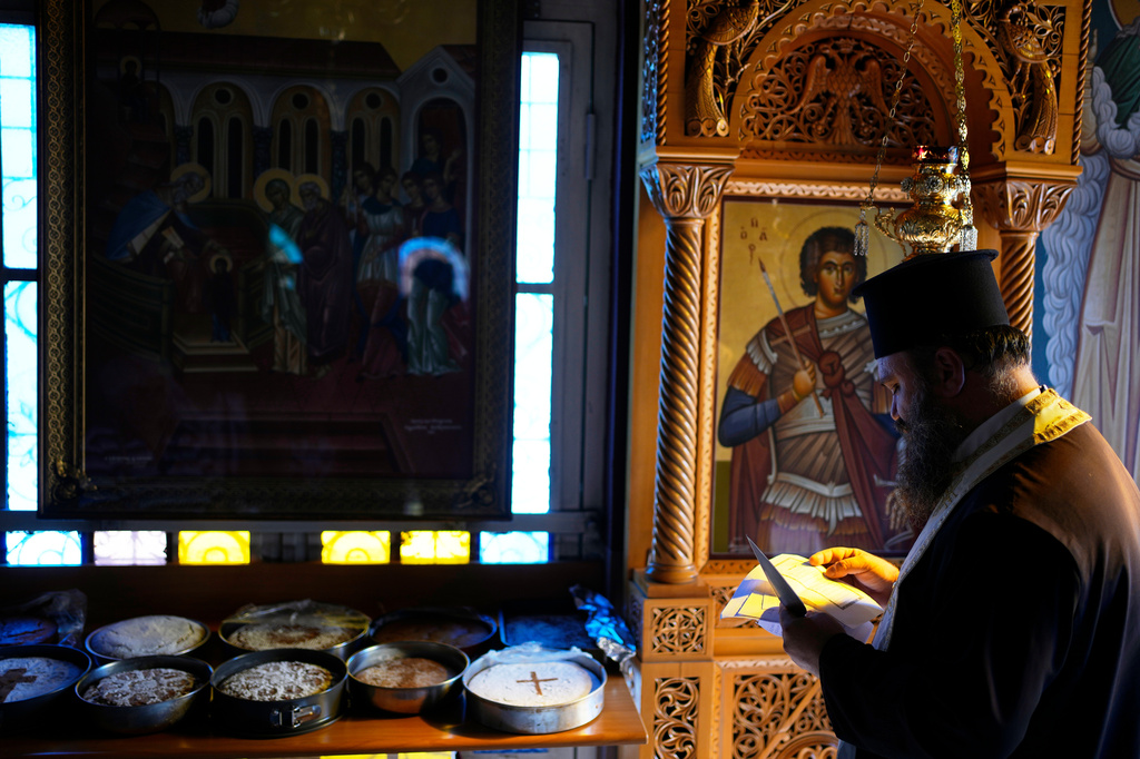 Father Nikolaos Vlavianos blesses the parishioners' Fanouropites, orange-flavored cakes, as an icon of Saint Fanourios, known in Greek as "The Revealer," is seen at right at the Church of St. Fanourios in Athens, Tuesday, Aug. 25, 2026. (AP Photo/Thanassis Stavrakis)