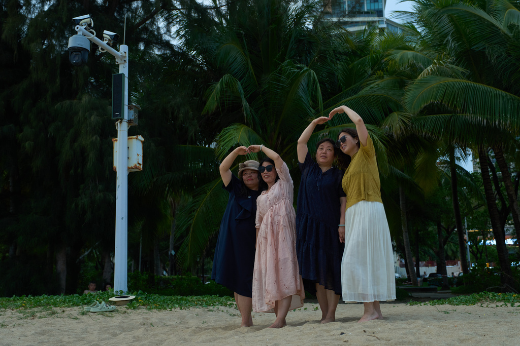 Tourists pose for photos near security cameras along a beach in Sanya city in southern China's Hainan province, Friday, April 25, 2025. (AP Photo/Ng Han Guan)