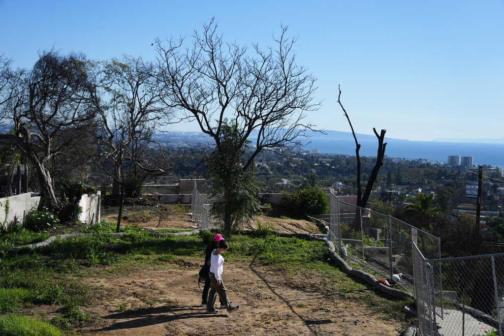 Starr Parodi, in pink hat, and her daughter Isolde Fair walk on their fire-ravaged property, which has been sold, on the one-year anniversary of the Palisades Fire in the Pacific Palisades neighborhood of Los Angeles Wednesday, Jan. 7, 2026. (AP Photo/Jae C. Hong)