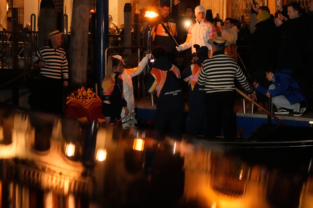 Torchbearers hold the Olympic torches flame on the Grand Canal in Venice, Italy, Thursday, Jan. 22, 2026, its journey will conclude in Milan on February 6 for the Winter Olympics opening ceremony. (AP Photo/Luca Bruno)