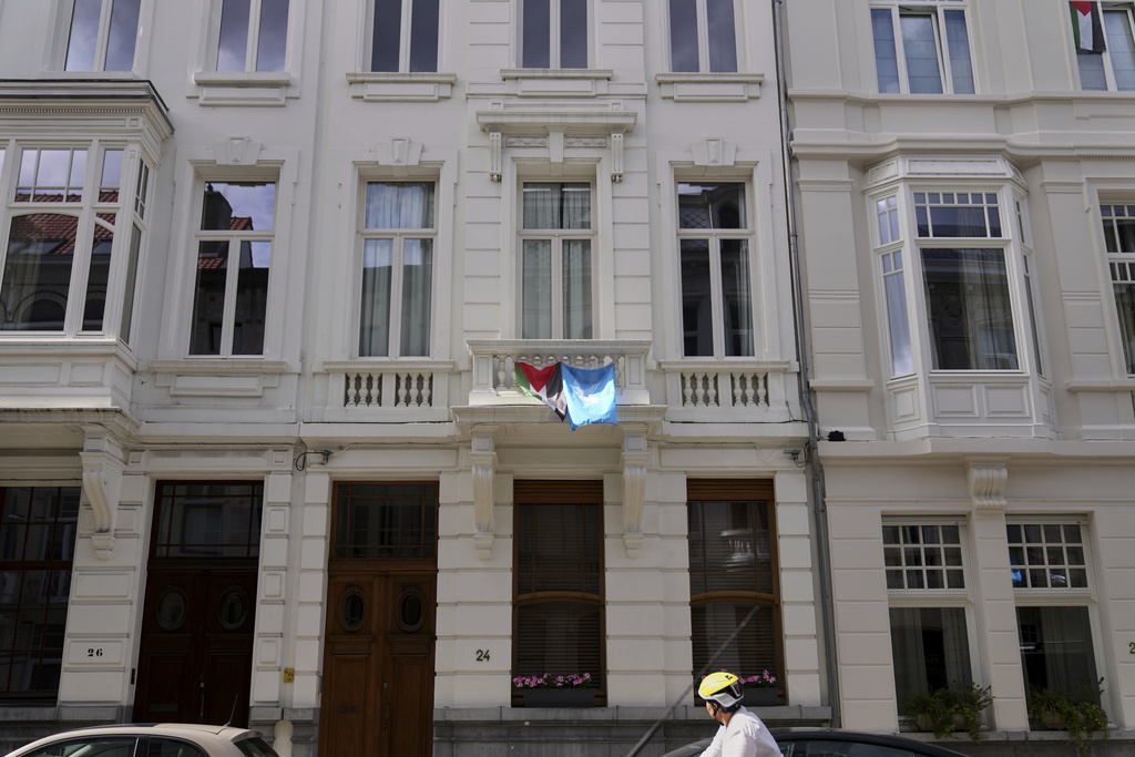 A cyclist looks up at a Palestinian and World Peace flag displayed from a balcony of a house in Antwerp, Belgium, Tuesday, Sept. 2, 2025. (AP Photo/Virginia Mayo)