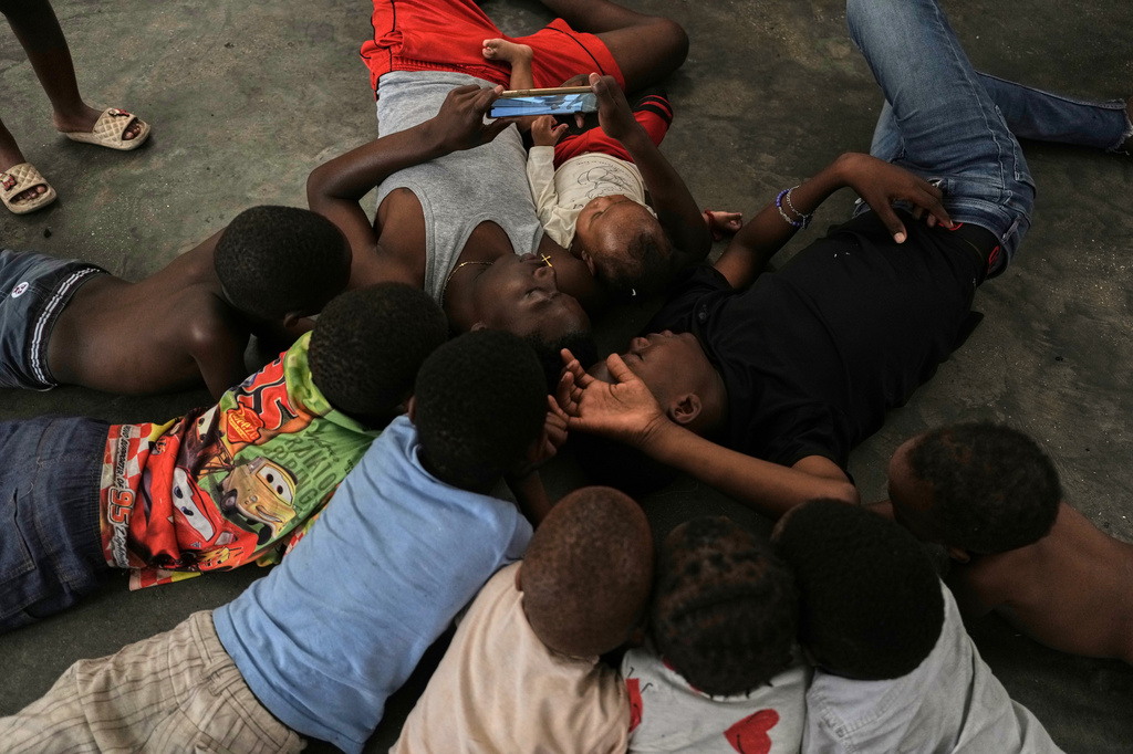 Children watch a movie on a mobile phone at a shelter for families displaced by gang violence in Port-au-Prince., Haiti, Friday, July 31, 2026. (AP Photo/Odelyn Joseph)