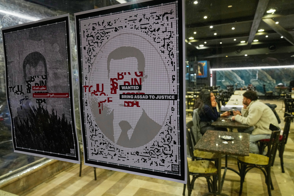 Wanted portraits of former Syrian president Bashar Assad are displayed in the window of a coffeeshop, in Damascus Sunday, Dec. 7, 2025, as Syrians celebrate marking the first anniversary of the ousting of the Bashar Assad regime. (AP Photo/Hussein Malla)