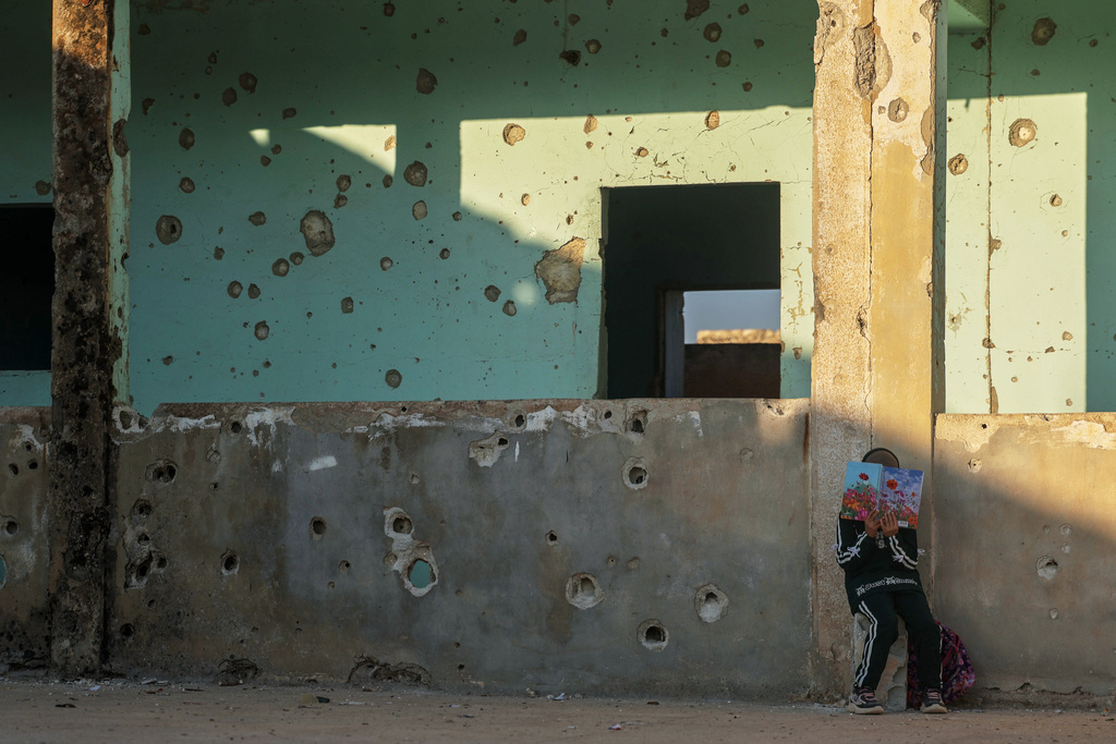 A student reads a book while leaning against a wall of the Maar Shmarin Primary School, its surface scarred by bullet holes from the fighting between forces loyal to former President Bashar Assad and rebel groups, in the village of Maar Shmarin, in the Idlib countryside, Syria, Sunday, Oct. 19, 2025. (AP Photo/Ghaith Alsayed)