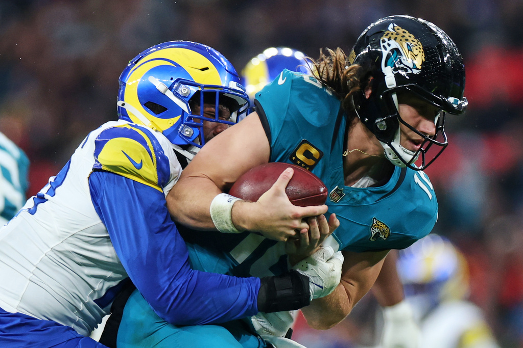 Jacksonville Jaguars quarterback Trevor Lawrence (16), right, is tackled by Los Angeles Rams Josaiah Stewart (10) during the second half of an NFL football game between the Los Angeles Rams and the Jacksonville Jaguars in London, Sunday, Oct. 19, 2025. (AP Photo/Ian Walton)