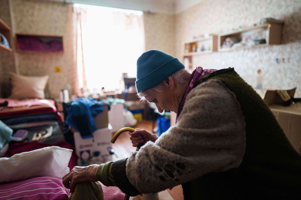 An elderly woman uses a cane to walk to her bed at a hostel for displaced people in Dnipro, Ukraine, Wednesday, Oct. 8, 2025. (AP Photo/Evgeniy Maloletka)