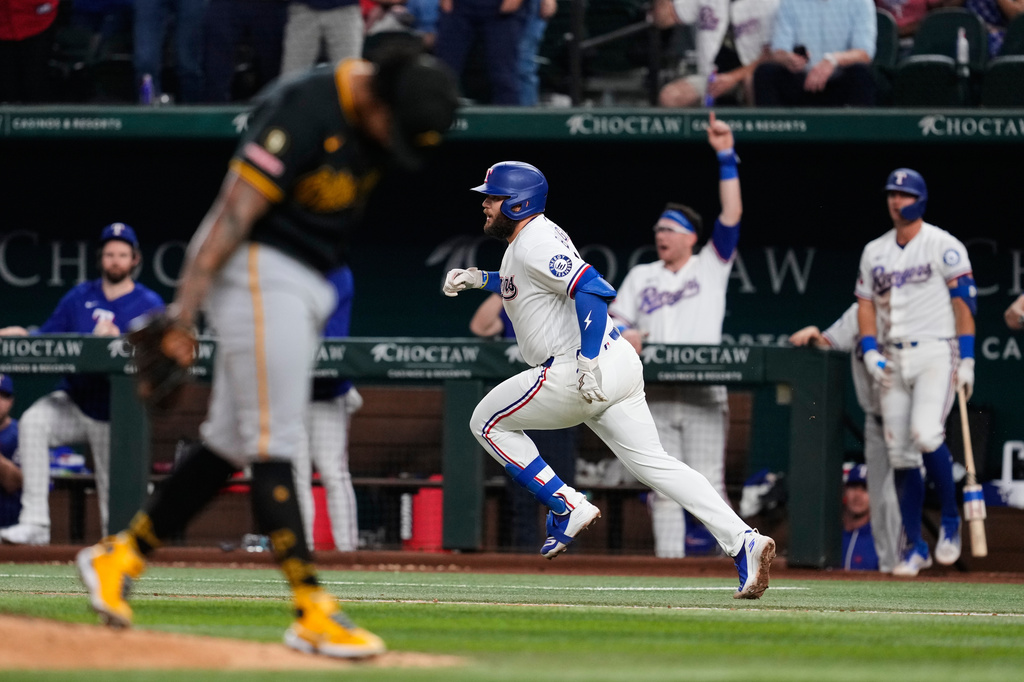 Texas Rangers' Jake Burger, center, sprints to first with a two-run single as Pittsburgh Pirates pitcher Gregory Soto, front left, reacts to the play in the eighth inning of a baseball game Wednesday, April 22, 2026, in Arlington, Texas. (AP Photo/Tony Gutierrez)