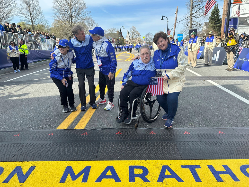 FILE - Four-time Boston Marathon winner Bill Rodgers and wheelchair athlete pioneer Bob Hall, second right, grand marshals of the 129th Boston Marathon, greet race volunteers at the start of the Boston Marathon, Monday April 21, 2025. (AP Photo/ Jennifer McDermott, File)