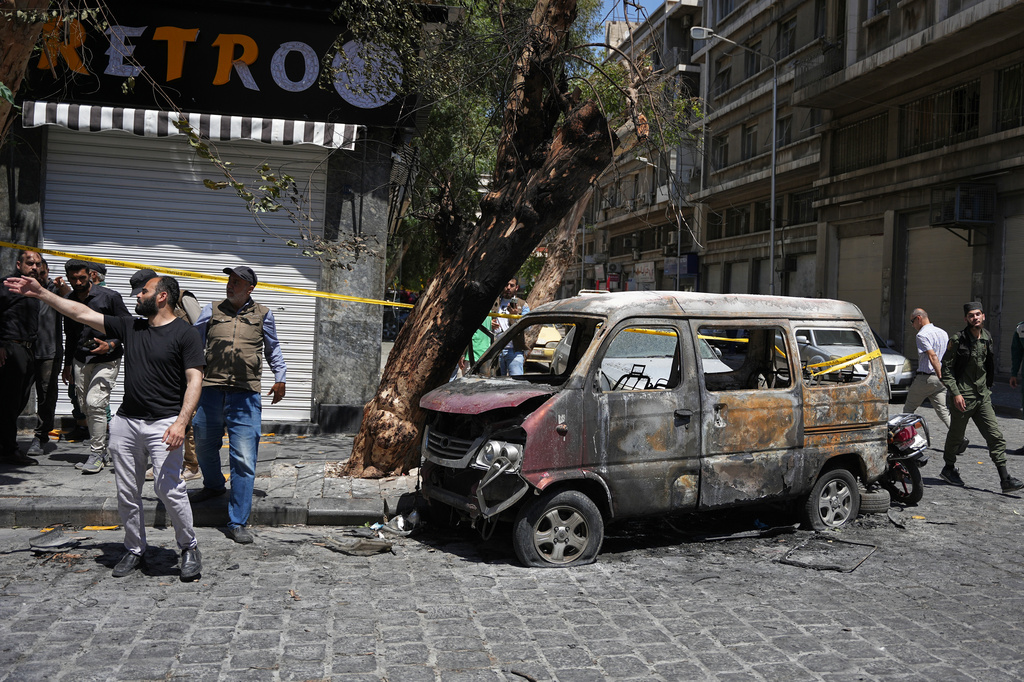 Syrian security personnel inspect a burned vehicle near the Four Seasons Hotel after two explosions rocked the area earlier while Syrian President Ahmad al-Sharaa was meeting French President Emmanuel Macron at the presidential palace, in Damascus, Syria, Tuesday, July 7, 2026. (AP Photo/Omar Albam)