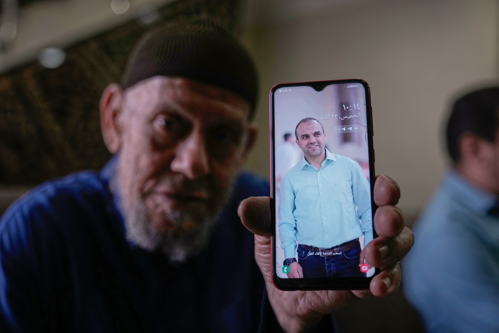 Waleed Husein Ali, shows a picture on a phone of his son, Mohammad, 45, who died in Israeli custody at the Kishon detention center, as he sits in the family's living room in the Nur Shams refugee camp near the West Bank town of Tulkarem, Thursday, Oct. 23, 2025. (AP Photo/Majdi Mohammed)