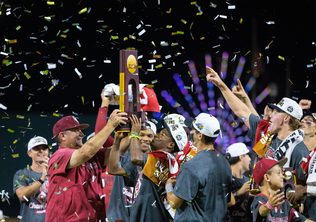 Oklahoma head coach Skip Johnson, front left, hands the championship trophy to Jason Walk, center, as they celebrate after their victory over North Carolina in Game 3 of the NCAA College World Series baseball finals in Omaha, Neb., Monday, June 22, 2026. (AP Photo/Rebecca S. Gratz)