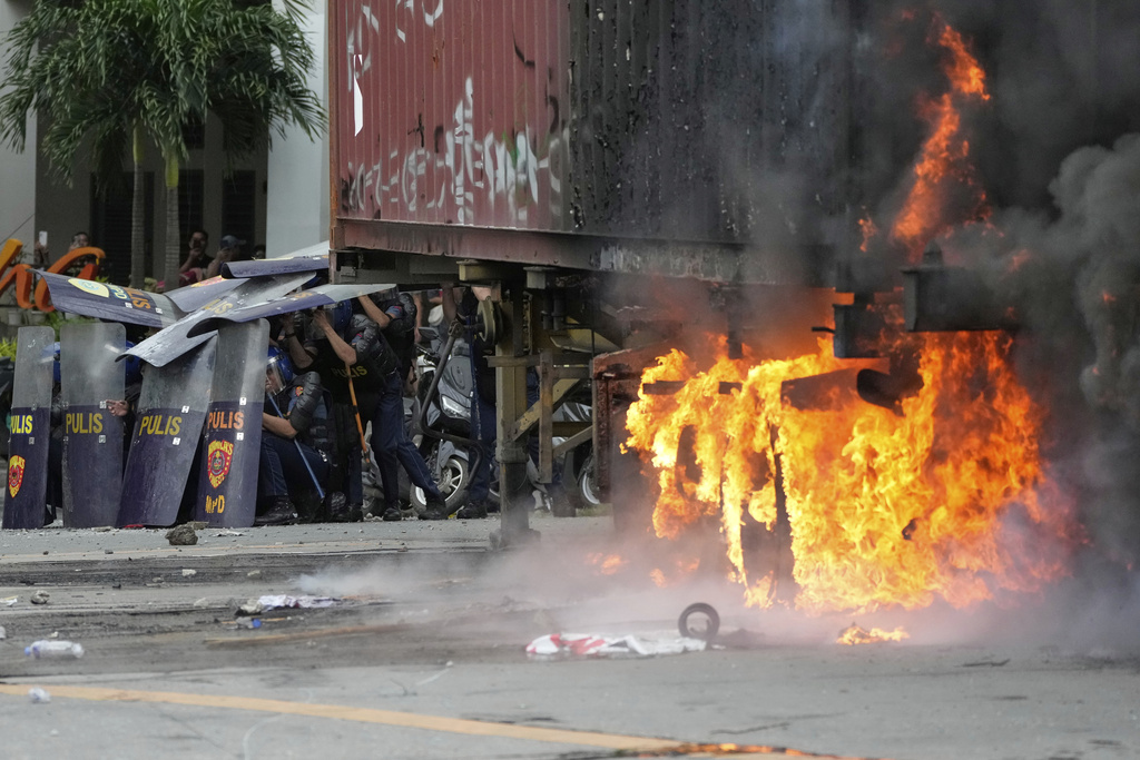 Police shield themselves beside a burning container during clashes with anti-corruption protesters in Manila, Philippines, Sunday, Sept. 21, 2025. (AP Photo/Aaron Favila)