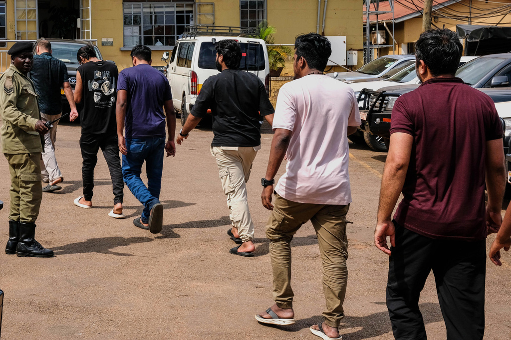 A Ugandan police officer escorts foreign nationals after authorities arrested dozens of foreigners in a crackdown on illegal migration, in Kampala, Uganda, Tuesday, April 28, 2026. (AP Photo/Hajarah Nalwadda)