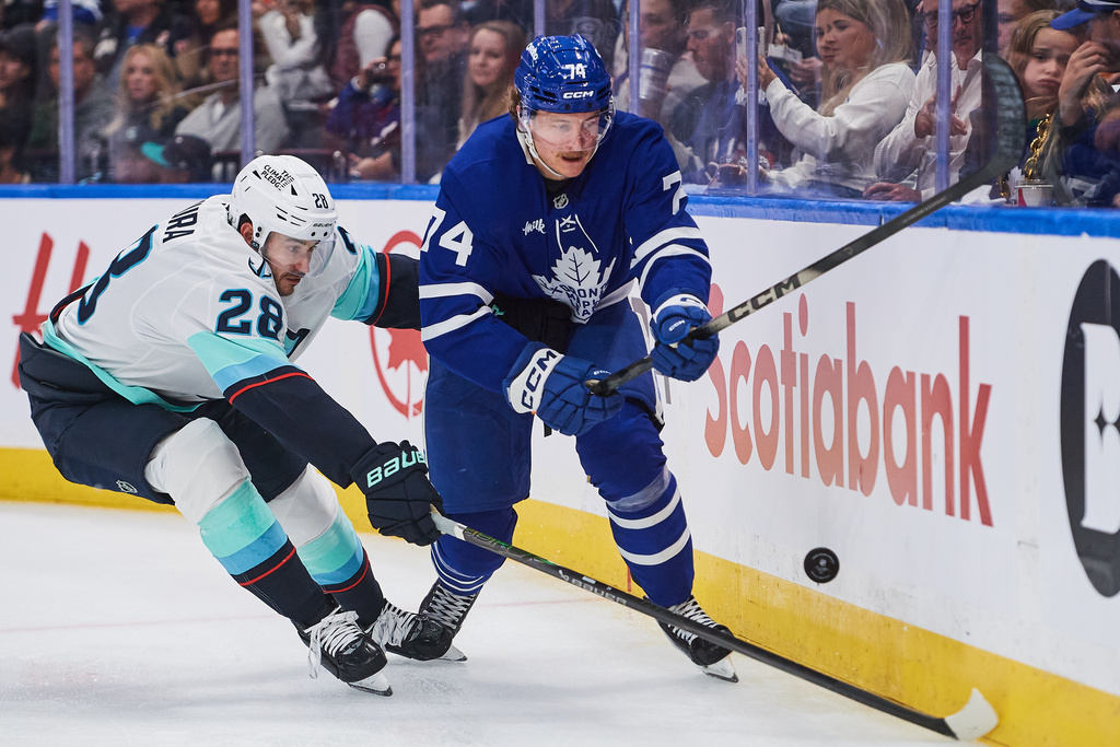 Seattle Kraken's Joshua Mahura (28) and Toronto Maple Leafs' Bobby McMann (74) battle for the puck during the second period of an NHL hockey game in Toronto on Saturday, Oct. 18, 2025. (Sammy Kogan/The Canadian Press via AP)