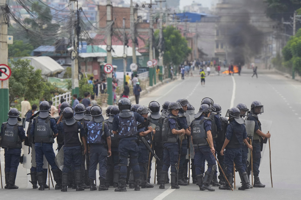 Policemen in riot gear stand guard on a street as protesters burn tires violating curfew orders in Kathmandu, Nepal, Tuesday, Sept. 9, 2025 after Nepal’s government lifted its ban on social media platforms after violent street protests. (AP Photo/Niranjan Shrestha)