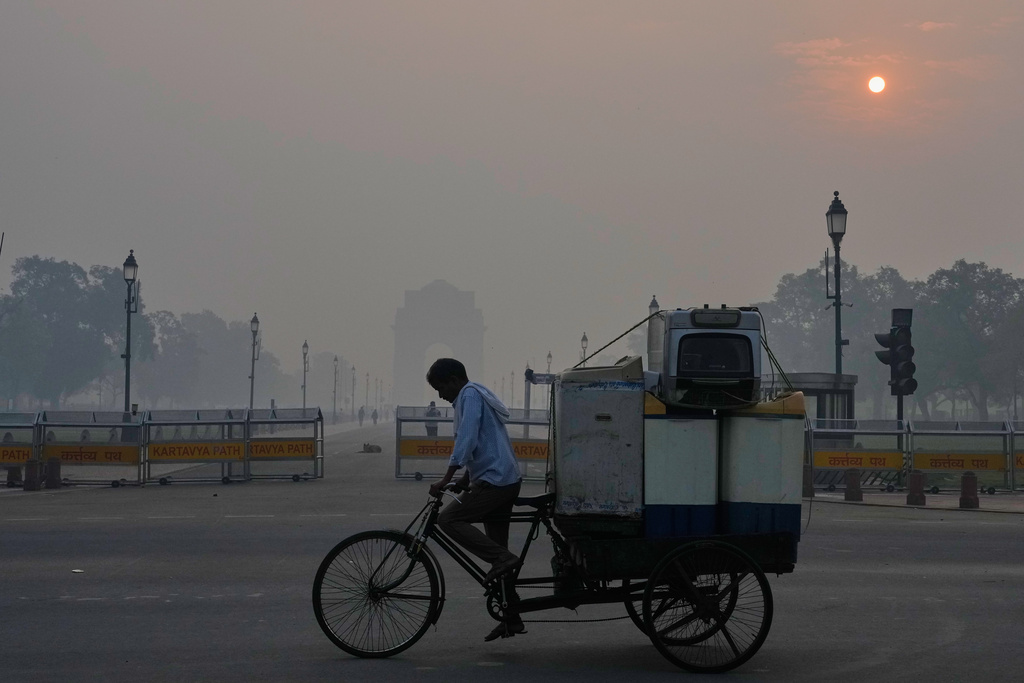FILE - A cyclist pedals through morning smog near the India Gate monument as he transports used home appliances in New Delhi, India, Oct. 21, 2025. (AP Photo/Manish Swarup, File)