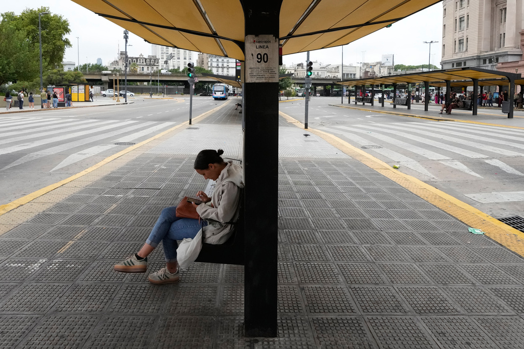 A woman sits at a bus stop that is empty due to a union strike against President Javier Milei’s proposed labor reform bill in Buenos Aires, Argentina, Thursday, Feb. 19, 2026. (AP Photo/Gustavo Garello)