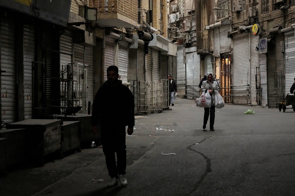 A woman carries her groceries as people walk along the mostly empty Tehran traditional main bazaar, where most shops are closed, in Tehran, Iran, Tuesday, March 10, 2026. (AP Photo/Vahid Salemi)