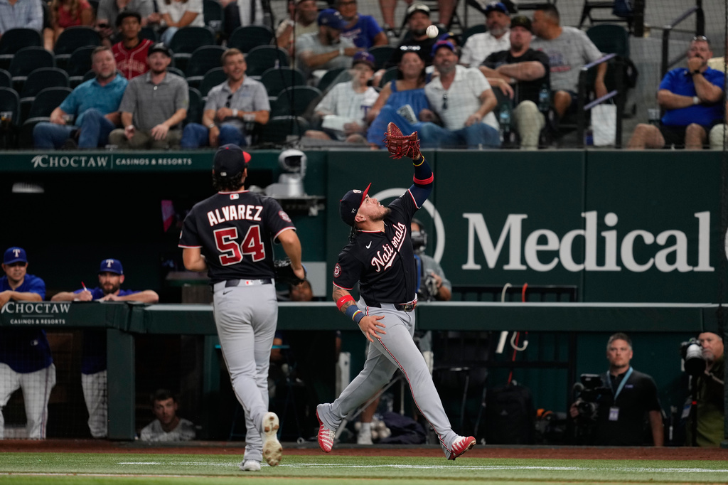 Washington Nationals first baseman Andrés Chaparro, right, reaches up to catch a pop out by Texas Rangers' Jake Burger as pitcher Andrew Alvarez (54) looks on in the fifth inning of a baseball game Thursday, Aug. 20, 2026, in Arlington, Texas. (AP Photo/Tony Gutierrez)