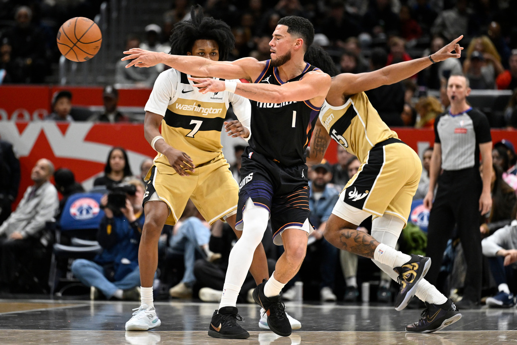 Phoenix Suns guard Devin Booker (1) passes off against Washington Wizards guard Bub Carrington (7) during the first half of an NBA basketball game, Monday, Dec. 29, 2025, in Washington. (AP Photo/John McDonnell)