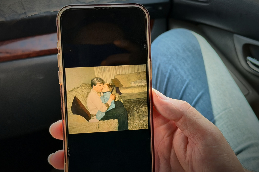 Erblin Ademi, right, whose father, Adem Ademi, a prominent surgeon, disappeared along with 22 other intellectuals during the Kosovo war in April 1999, shows a photo of him and his father, near the excavation site of a mass grave in Small Kalluder, Kosovo, Wednesday, Aug. 5, 2026. (AP Photo/Zana Cimili)