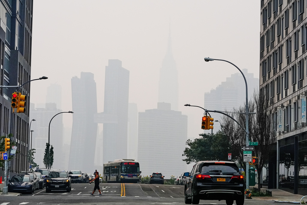 Pedestians cross Borden Avenue as the New York City skyline is obscured during poor air quality due to smoke from Canadian wildfires Thursday, July 16, 2026, in the Queens borough of New York. (AP Photo/Frank Franklin II)
