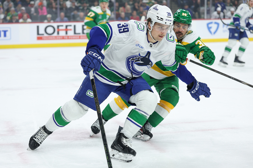 Vancouver Canucks center Ty Mueller (39) skates with the puck ahead of Minnesota Wild right wing Mats Zuccarello (36) during the first period of an NHL hockey game Thursday, April 2, 2026, in St. Paul, Minn. (AP Photo/Matt Krohn)
