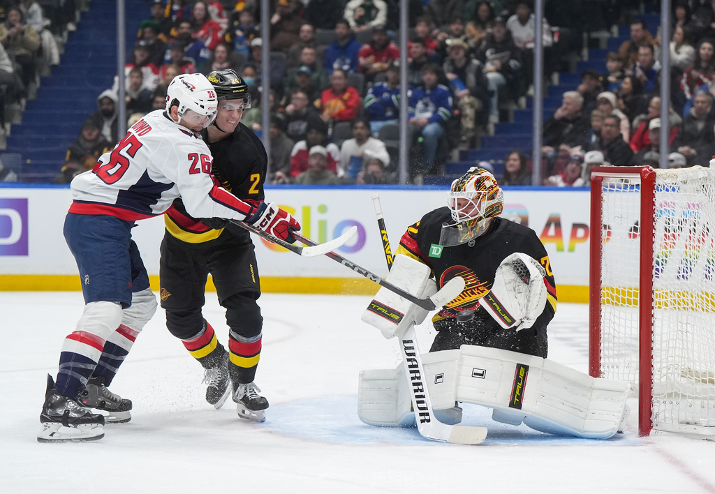 Vancouver Canucks goalie Kevin Lankinen, right, makes the save as Washington Capitals' Nic Dowd (26) gets his stick on the puck while Vancouver's Zeev Buium (24) defends during the first period of an NHL hockey game in Vancouver, British Columbia, Wednesday, Jan. 21, 2026. (Darryl Dyck/The Canadian Press via AP)
