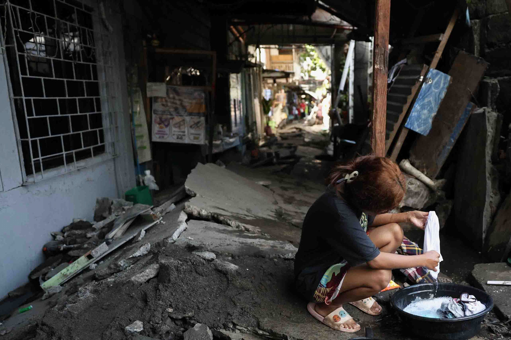 A woman washes clothes along a damaged pathway in General Santos, southern Philippines, Thursday, June 11, 2026, following Monday's powerful earthquake. (AP Photo/Basilio Sepe)