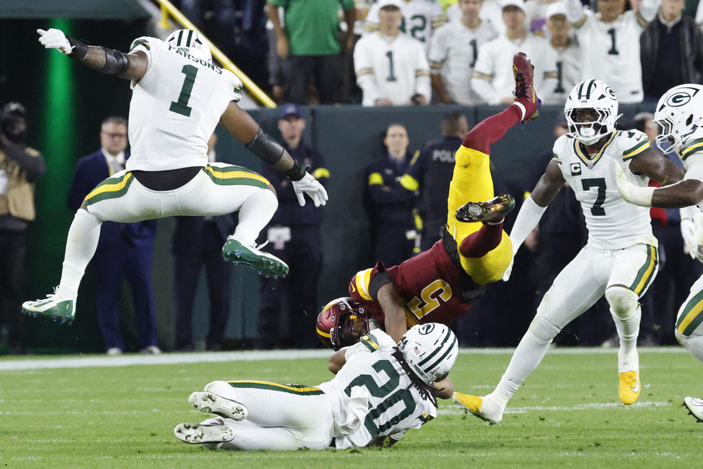 Washington Commanders quarterback Jayden Daniels (5) is upended by Green Bay Packers safety Javon Bullard (20) as Packers defensive lineman Micah Parsons (1) and linebacker Quay Walker (7) watch during the second half of an NFL football game Thursday, Sept. 11, 2025, in Green Bay, Wis. (AP Photo/Mike Roemer)