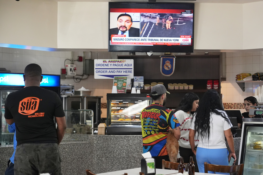 People order food at El Arepazo, a popular restaurant in the local Venezuelan community, as a television broadcast shows Venezuelan President Nicolas Maduro being led from a helicopter to a court appearance in New York, Monday, Jan. 5, 2026, in Doral, Fla. (AP Photo/Lynne Sladky)