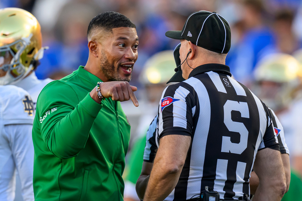 Notre Dame head coach Marcus Freeman, left, has a discussion with sideline judge Chris Junjulas, right, during the first half of an NCAA college football game against BYU, Saturday, Oct. 17, 2026, in Provo, Utah. (AP Photo/Tyler Tate)