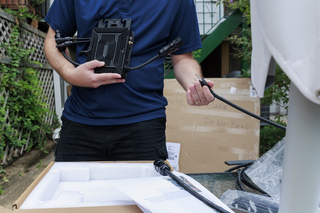 Craig Keenan prepares to install a microinverter with his solar panel from Bright Saver on Friday, Aug. 1, 2025, in Baltimore. (AP Photo/KT Kanazawich)
