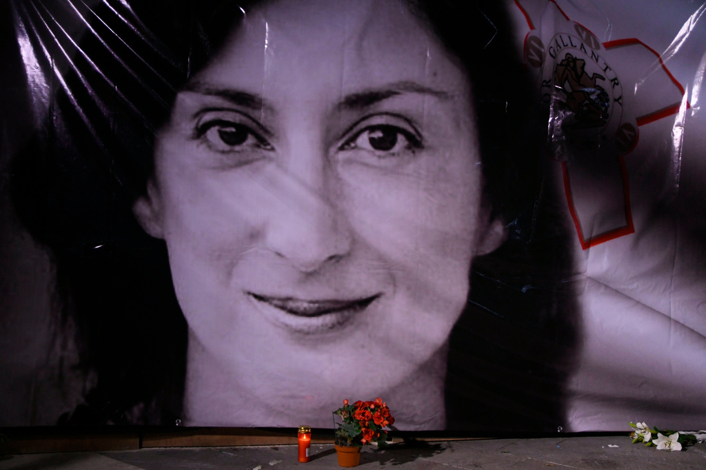 FILE - Flowers and a candle lie in front of a portrait of slain investigative journalist Daphne Caruana Galizia during a vigil outside the law courts in Valletta, Malta, Oct. 16, 2018. (AP Photo/Jonathan Borg, File)
