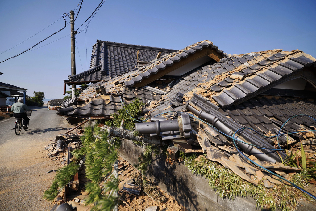 A person rides a bicycle past damaged buildings in Hikawa, southern Japan, Sunday, Aug. 2, 2026, following a July 28 earthquake. (Taichi Nagahisa/Kyodo News via AP)